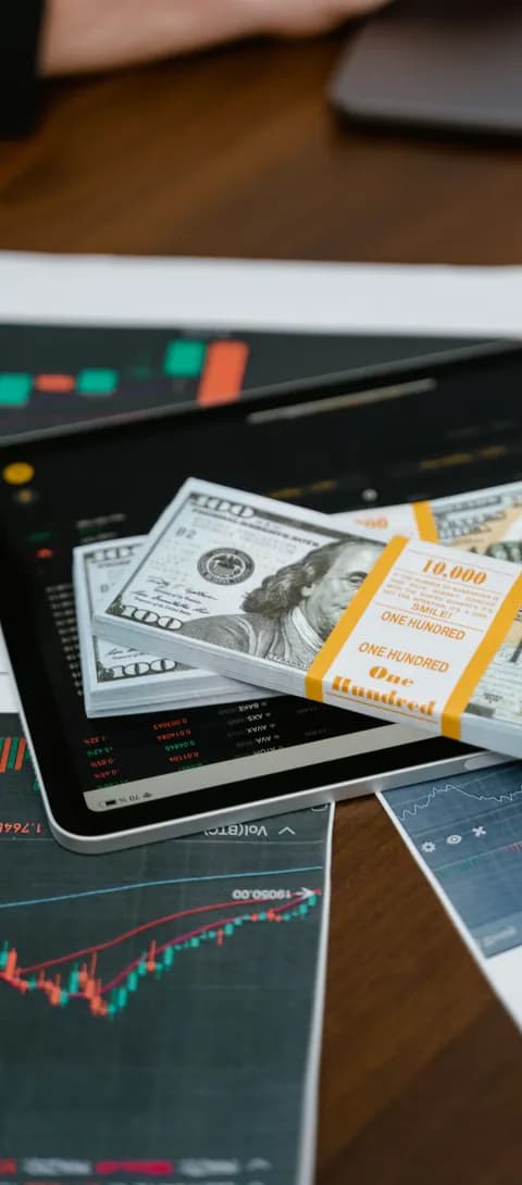 A tablet showing market performance charts beside banded cash on a desk